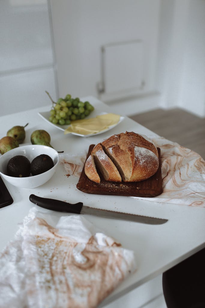 A cozy kitchen scene with freshly sliced bread, fruits, and a knife on the table. Perfect for food enthusiasts.