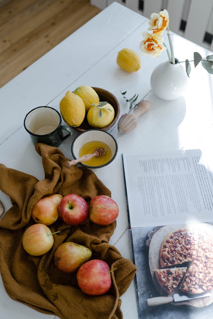 A cozy setup with fruits, honey, and a cookbook on a wooden table.