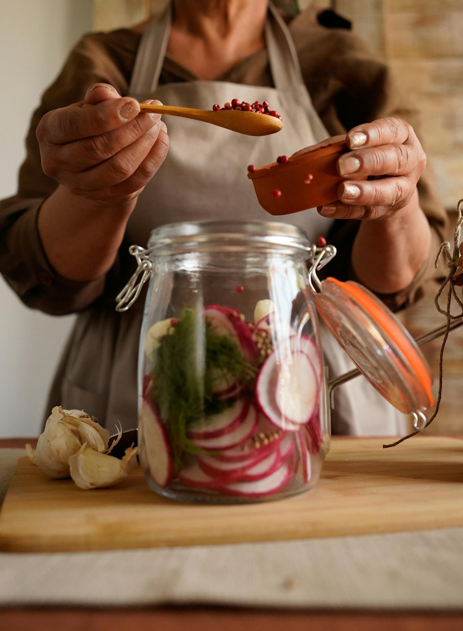 Hands preparing pickled vegetables in a jar with garlic on wooden board.