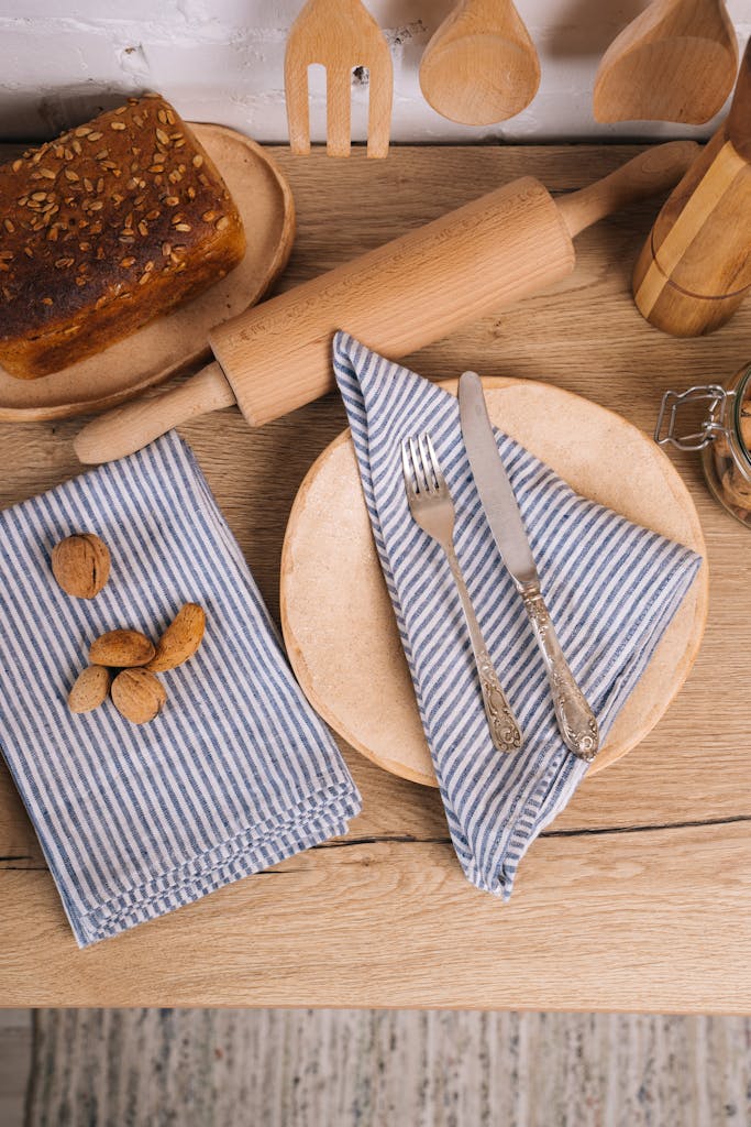 Top view of a cozy kitchen setting with bread, nuts, and utensils on a wooden table.