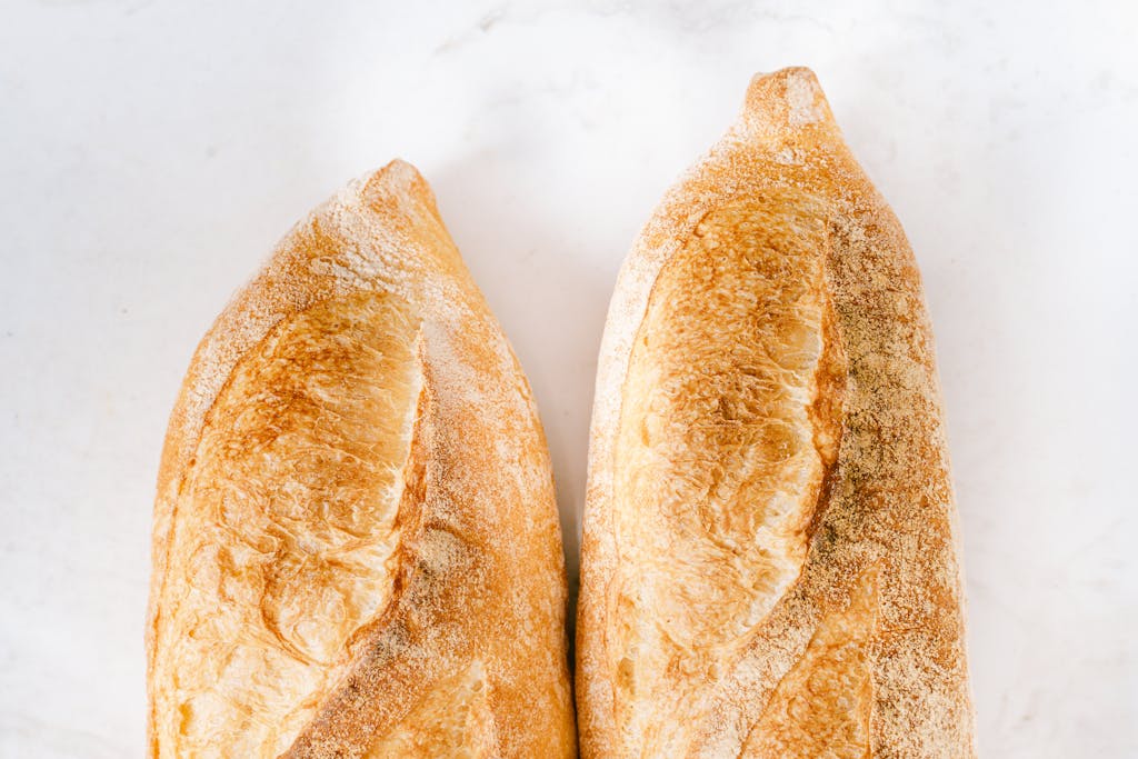 Two freshly baked baguettes on a white surface, showcasing golden crispy crust.