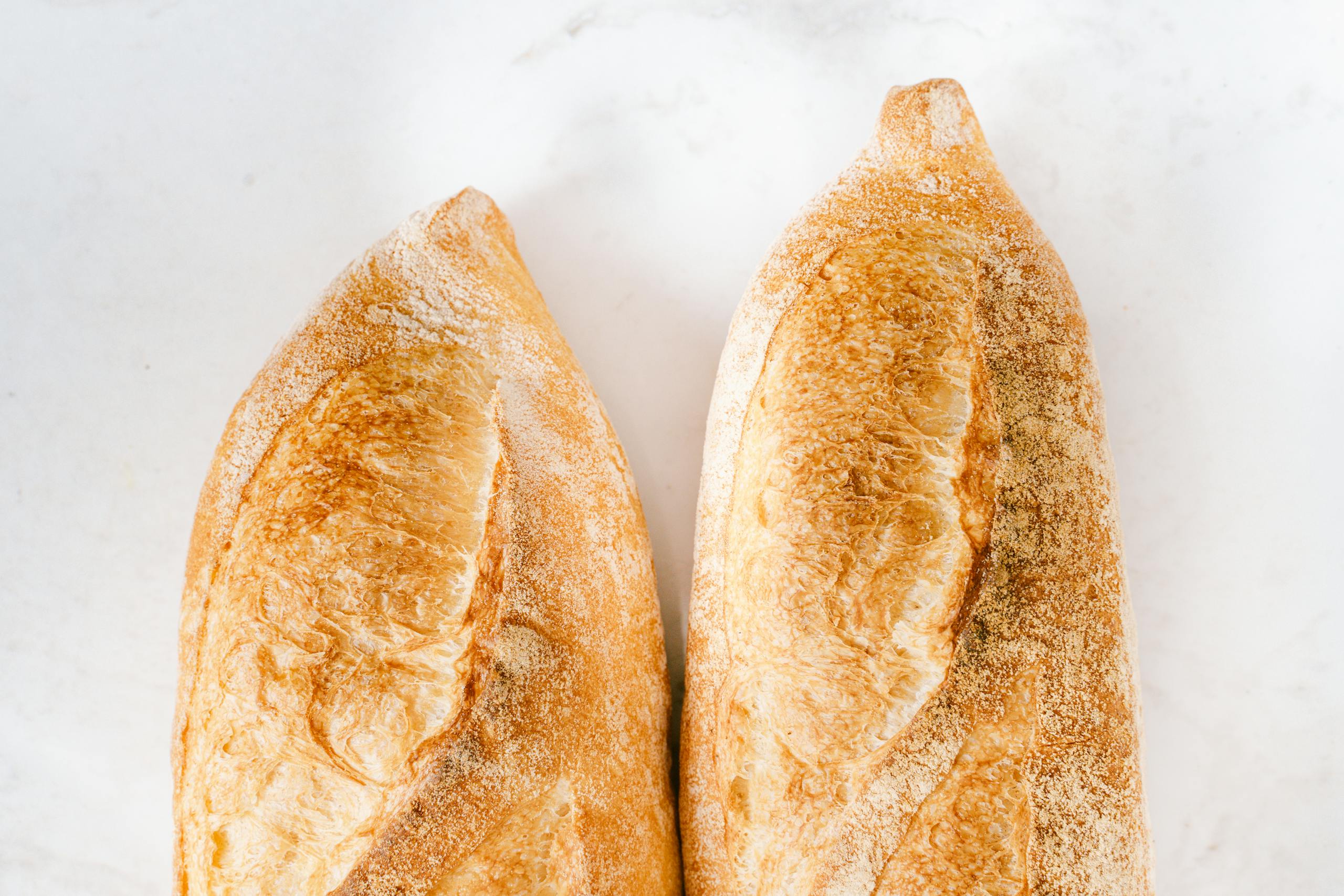 Two freshly baked baguettes on a white surface, showcasing golden crispy crust.