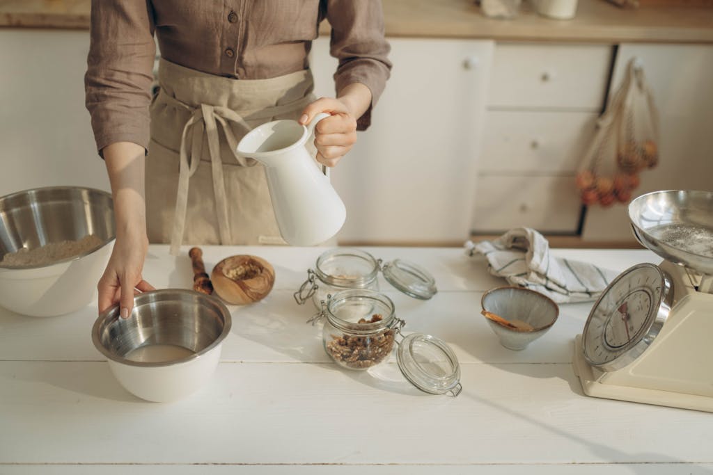 Woman pouring milk into a bowl with various baking ingredients on a kitchen counter.